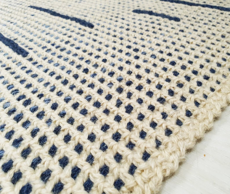 May include: Close-up of a woven rug with a natural beige background and blue stripes. The rug is made of a natural fiber and has a textured surface.