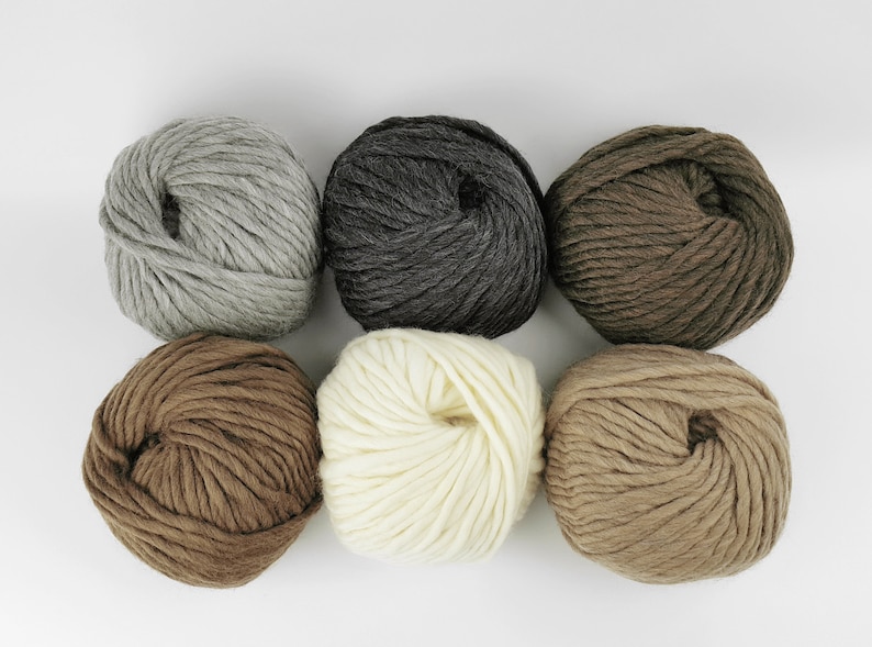 May include: Six balls of yarn in various shades of brown, grey, and white. The yarn is arranged in a circle on a white background.