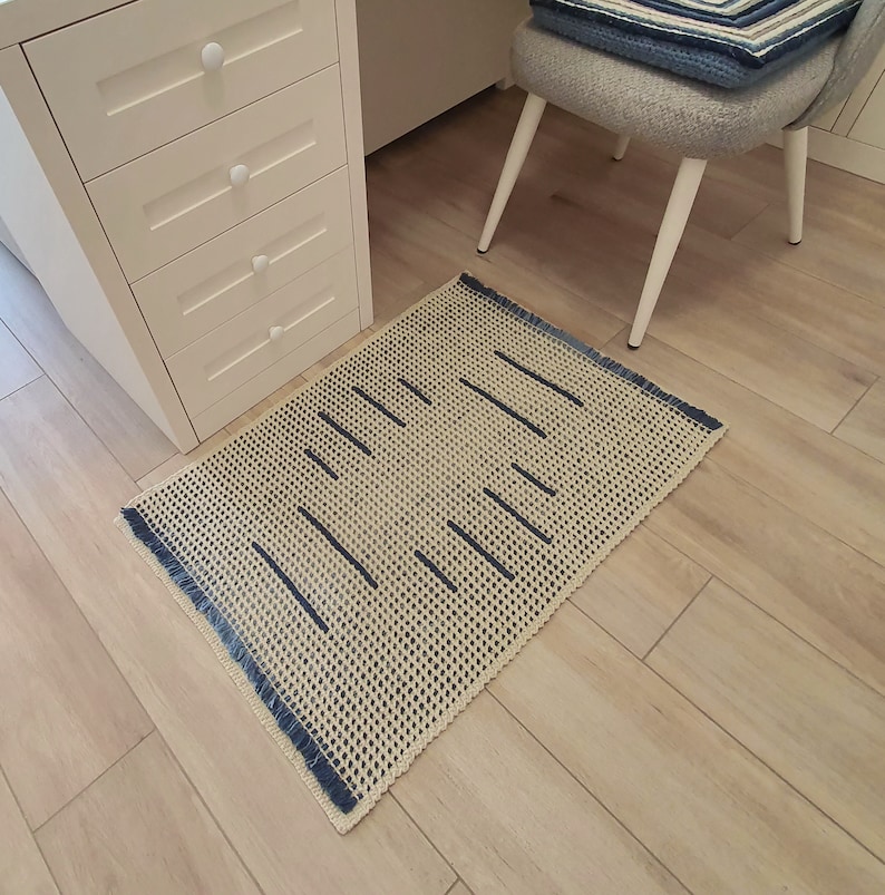 May include: A beige and blue woven rug with a fringe border. The rug has a geometric pattern of thin blue lines on a beige background.