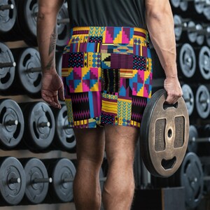 May include: A person wearing colorful athletic shorts with a geometric pattern. The shorts are made of a stretchy fabric and have a drawstring waistband. The person is holding a weight plate in their right hand.
