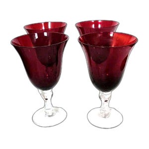 May include: Four ruby red wine glasses with a tulip-shaped bowl and a clear stem and base. The glasses are arranged in a square formation, showcasing their elegant design and rich color. Perfect for serving wine.