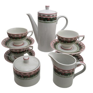 Puede incluir: Un juego de té de cerámica blanca con un diseño navideño festivo. El juego incluye una cafetera, una jarra de crema, un azucarero y varias tazas de té con platillos. El diseño presenta un patrón de acebo y bayas rojas y verdes.
