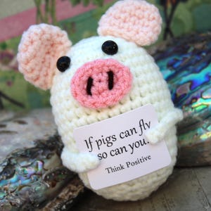 May include: A white crocheted pig holding a card that says "If pigs can fly so can you. Think Positive".
