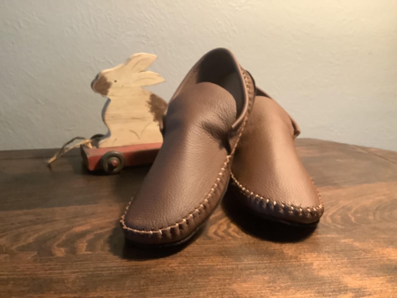 May include: A pair of brown leather moccasins with a decorative stitch around the edge.
