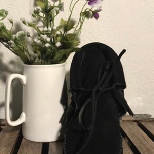 May include: Black suede moccasin with a decorative stitch around the sole and a leather tie closure.