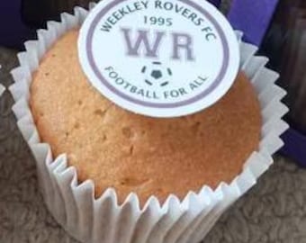 May include: A white cupcake topped with a purple and white logo. The logo reads "Weekley Rovers FC 1995 WR Football for All".