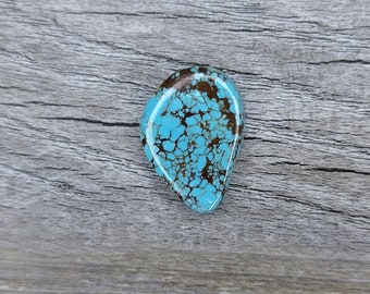 Può includere: Un cabochon turchese con una matrice marrone. La pietra ha una forma a goccia e una superficie liscia e lucida.