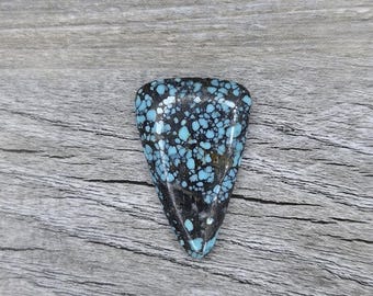 May include: A triangular piece of turquoise cabochon with a black matrix and blue and green veins. The stone has a speckled pattern.
