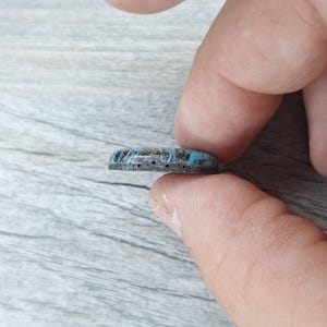 May include: A close-up side view of a round, blue and black cabochon with a textured surface and small holes around the edge.