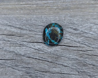 May include: A round, blue and black gemstone with a swirling pattern. The gemstone is on a light brown wooden surface.