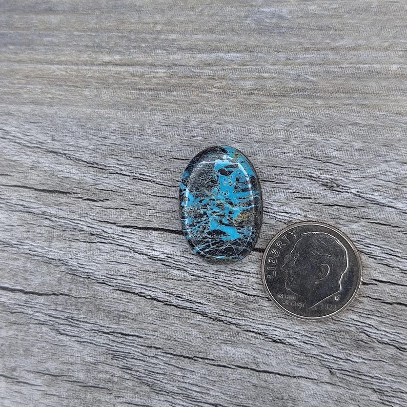 May include: A blue and black oval cabochon gemstone with a swirling pattern. The gemstone is about the size of a US dime.