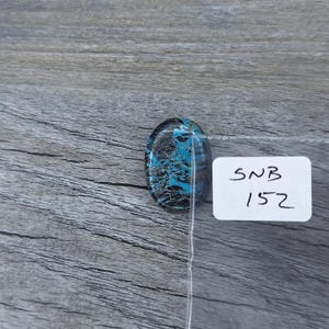 May include: A close-up of a blue and black oval cabochon gemstone with a white label that says "SNB 1572".