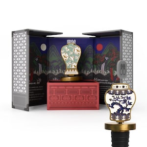 May include: Decorative bottle stoppers with a porcelain vase design. One stopper features a blue and white floral pattern, while the other has a green and gold design. The stoppers are displayed in a box with a Korean landscape scene.