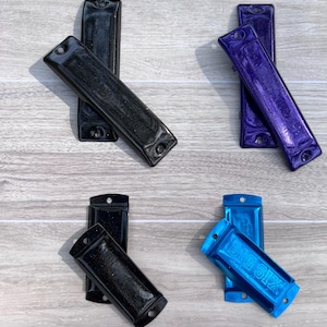 May include: Four harmonicas in black, purple, and blue, arranged in pairs. The blue harmonica has the text "BIG SIX". Each harmonica has a rectangular shape with rounded edges and holes at each end.
