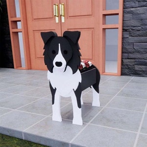 May include: A black and white wooden dog planter, resembling a Border Collie, stands on a tiled surface. The planter has a rectangular container for flowers, with red and white blooms visible. The dog-shaped planter is a decorative garden accent.