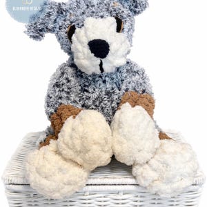 May include: A handmade plush dog toy with a blue, gray, and white color scheme. The dog has a white face and paws, brown accents, and is sitting on a white wicker basket. The logo "BLUEKREEK DESIGNS" is in the upper left corner.