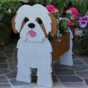 May include: A wooden dog-shaped planter with a white body, brown ears, and a pink tongue. The planter holds colorful flowers and is placed on a tiled surface. The dog planter is a decorative item for gardens.