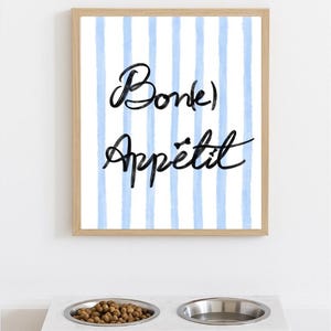 Peut inclure: Un cadre avec l'inscription « Bon Appétit » sur un fond à rayures bleues est suspendu au-dessus d'un bol pour animaux de compagnie en marbre avec deux inserts en acier inoxydable. Un bol est rempli de nourriture pour animaux.