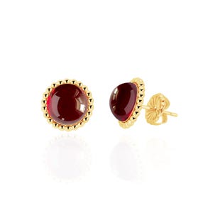 May include: A pair of stud earrings featuring a round, deep red gemstone set in a gold-colored, scalloped bezel. The earrings have a post and butterfly backing. The gemstones are a rich, dark red color.