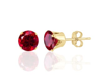 May include: A pair of gold stud earrings with a red round gemstone in the centre.
