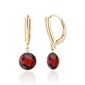May include: A pair of gold dangle earrings with red gemstone drops. The earrings have a lever back closure.