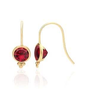 May include: A pair of gold earrings with a red gemstone in the center. The earrings are drop style and have a simple design.