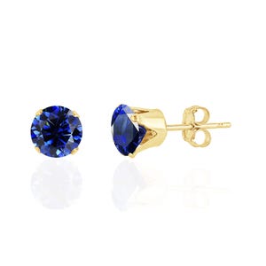 May include: A pair of stud earrings featuring round, faceted, deep blue stones set in four-prong yellow gold settings. One earring is shown from the front, while the other is displayed from the side, revealing the post and the butterfly back closure.