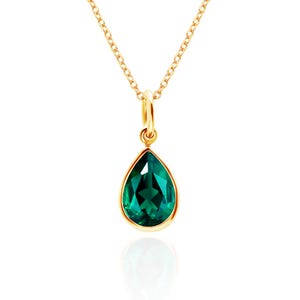 May include: A gold-colored necklace with a teardrop-shaped, emerald-green pendant. The pendant is set in a gold bezel and hangs from a delicate gold chain. The pendant's facets reflect light, creating a sparkling effect.
