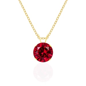 May include: A gold-colored chain necklace with a round, faceted, deep red gemstone pendant. The pendant is the focal point, reflecting light. The chain is delicate, and the pendant is suspended in the center, creating a classic jewelry piece.