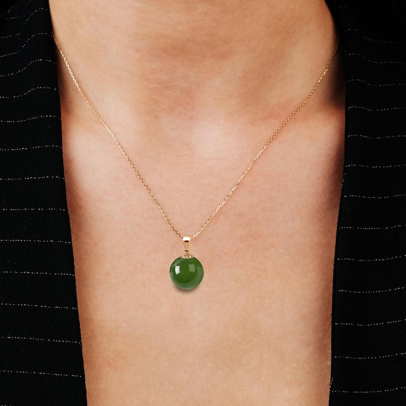 May include: A gold chain necklace with a green jade pendant. The pendant is round and smooth.