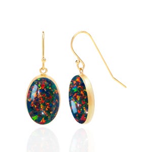 May include: A pair of gold drop earrings featuring oval-shaped cabochon opals. The stones display a dark base color with vibrant flashes of red, green, and blue. Each opal is set in a smooth gold bezel and hangs from a simple gold hook wire.