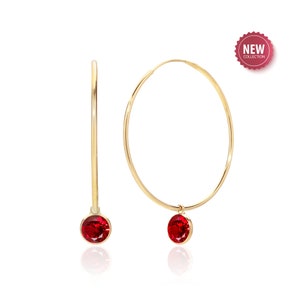 May include: Gold hoop earrings with a dangling red gemstone.  The earrings are part of a new collection.