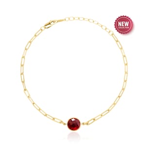 May include: A gold chain bracelet with a red gemstone pendant.  The bracelet is made of a delicate chain and has a lobster clasp closure.  The gemstone is round and has a faceted cut.  The bracelet is a new design.
