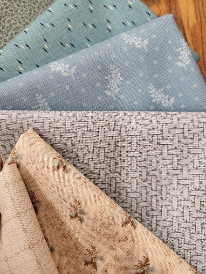 May include: A collection of folded fabric swatches featuring various patterns. The stack includes a light blue fabric with white floral prints, a blue fabric with dark dashes, a beige fabric with a woven grid, and a beige fabric with small floral motifs.