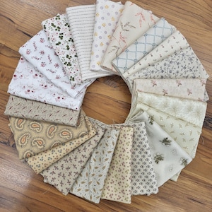May include: A circular arrangement of folded fabric squares featuring various patterns including floral prints, paisley, geometric grids, stripes, and small botanical motifs in shades of cream, beige, brown, green, and muted red.