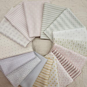 May include: A collection of folded fabric swatches arranged in a circular pattern. The fabrics feature various patterns, including dots, stripes, and floral designs, in shades of white, pink, gray, and yellow. The fabrics are likely cotton or linen.