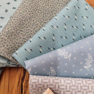 May include: A collection of folded fabric squares featuring various patterns including small floral prints, delicate leaf motifs, a geometric basket-weave design, and a light blue fabric with small dark and light dashes arranged in a repeating pattern.