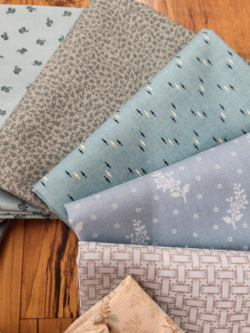 May include: A collection of folded fabric squares featuring various patterns including small floral prints, delicate leaf motifs, a geometric basket-weave design, and a light blue fabric with small dark and light dashes arranged in a repeating pattern.