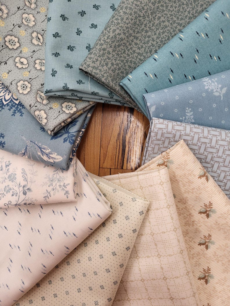 May include: A collection of folded fabric swatches arranged in a circular pattern, featuring various patterns including floral prints, geometric grids, small dots, and dashes in shades of light blue, sage green, cream, and beige.