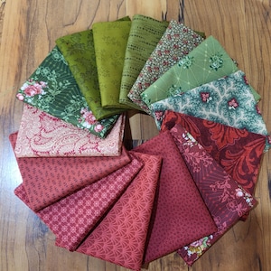 May include: A collection of folded fabric squares arranged in a circular fan pattern. The textiles feature a variety of patterns including floral, paisley, geometric, and botanical prints in shades of deep red, burgundy, olive green, and sage.