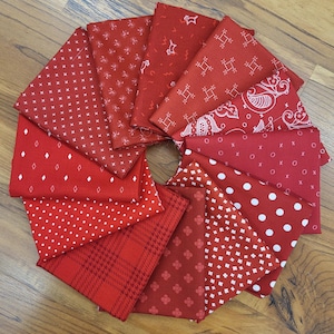 May include: A collection of twelve folded fabric squares arranged in a circular fan pattern. Each square is a shade of red with a unique white printed pattern, including polka dots, diamonds, crosses, paisley, plaid, and small geometric shapes.