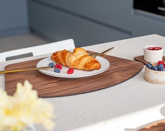 May include: A wooden serving tray with a white plate containing a croissant, blueberries, and raspberries. The tray is on a white tablecloth with a glass bowl of fruit and a small bowl of red jam.
