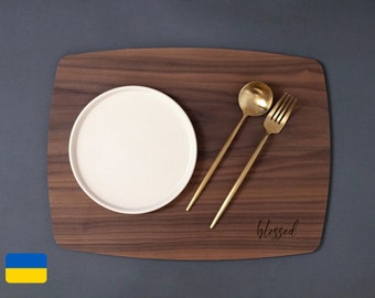 May include: A wooden placemat with a white plate, a gold fork, and a gold spoon. The placemat has the word "blessed" engraved on it.