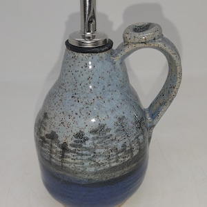May include: A blue and white ceramic oil and vinegar bottle with a black stopper and a silver spout. The bottle has a speckled glaze and a handle.