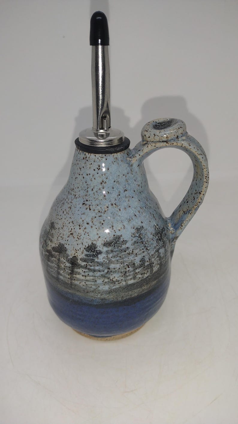 May include: A blue and white ceramic oil and vinegar bottle with a black stopper and a silver spout. The bottle has a speckled glaze and a handle.