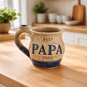 May include: A set of three ceramic mugs with a speckled, matte finish. The mugs are in shades of cream, light gray, and dark gray. Each mug has a simple, minimalist design and a rounded handle.