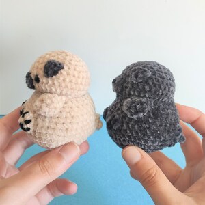 May include: Two crocheted plush toys shaped like pugs. One is beige and the other is gray.