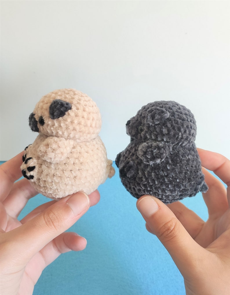 May include: Two crocheted plush toys shaped like pugs. One is beige and the other is gray.