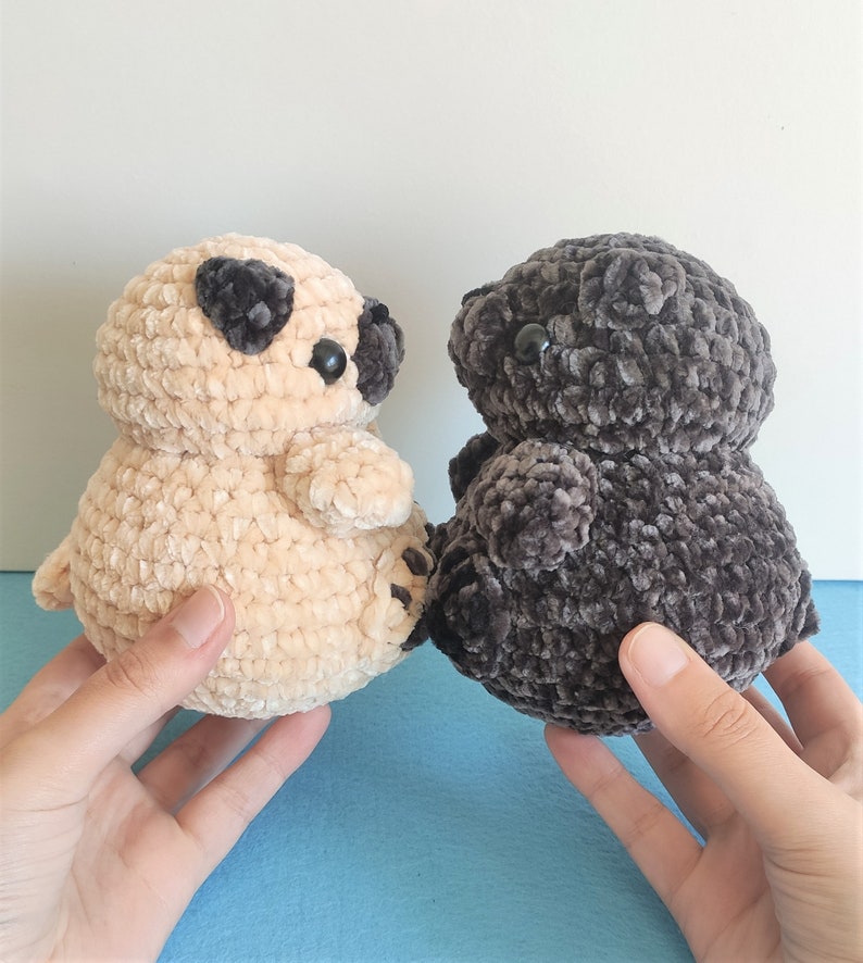 May include: Two crocheted plush toys shaped like pugs. One is beige and the other is dark gray.