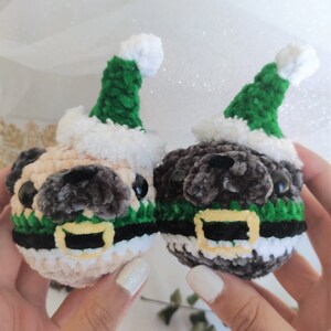 Pu&ograve; includere: Due pugs di peluche all'uncinetto che indossano cappelli di Babbo Natale verdi e bianchi con cinture nere e gialle.